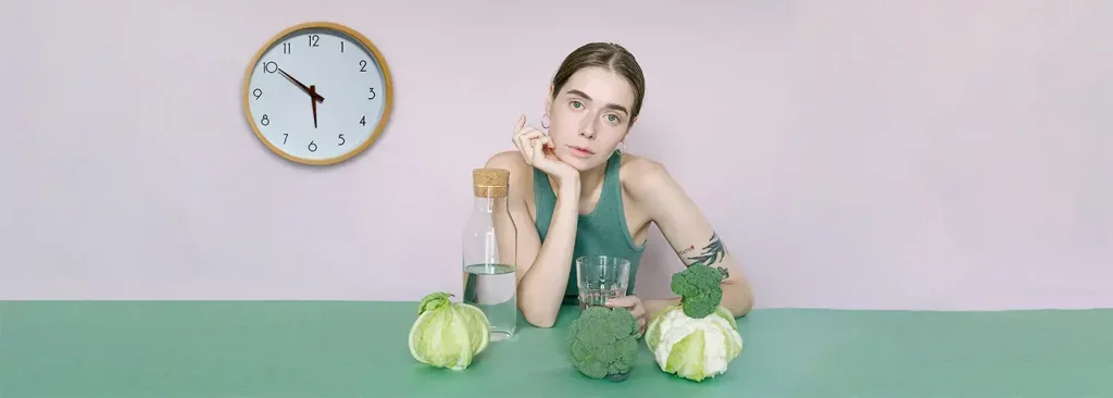 Persona sentada a una mesa con verduras y un reloj en la pared