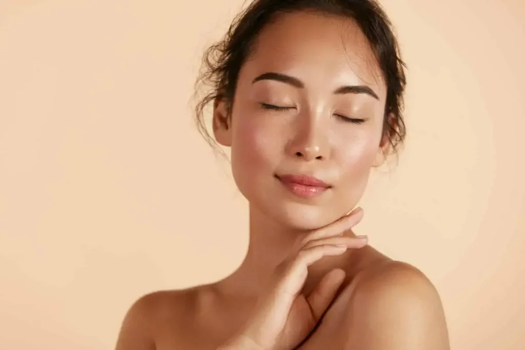 Mujer de piel limpia con los ojos cerrados en un fondo de color beige.